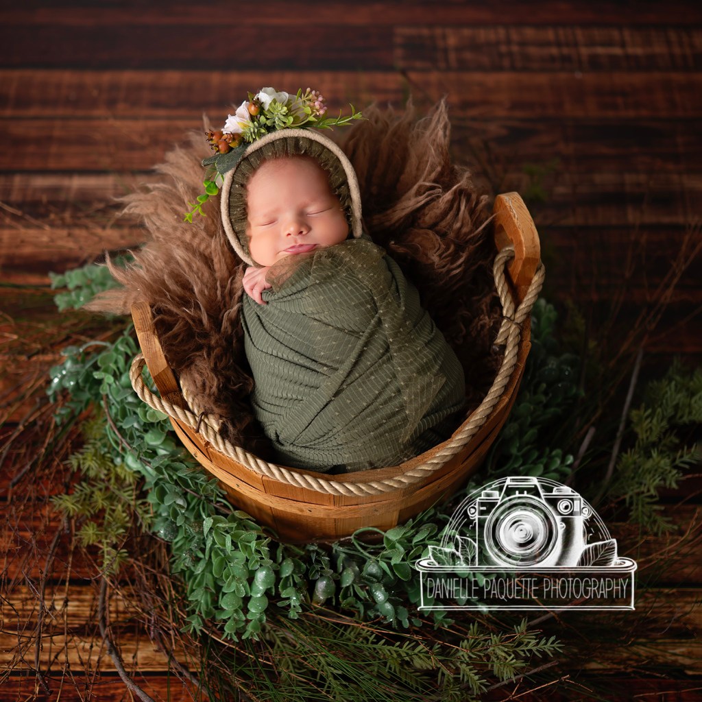 Sweet snuggly newborn in basket with woodland features